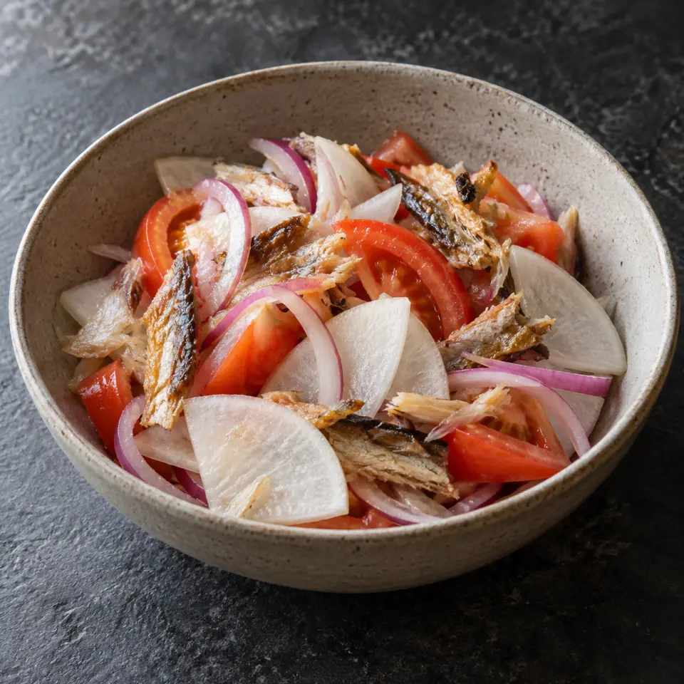 Radish Ensalada in a wide bowl on a dark stone table, made with tomatoes, red onion, daikon, dried fish.